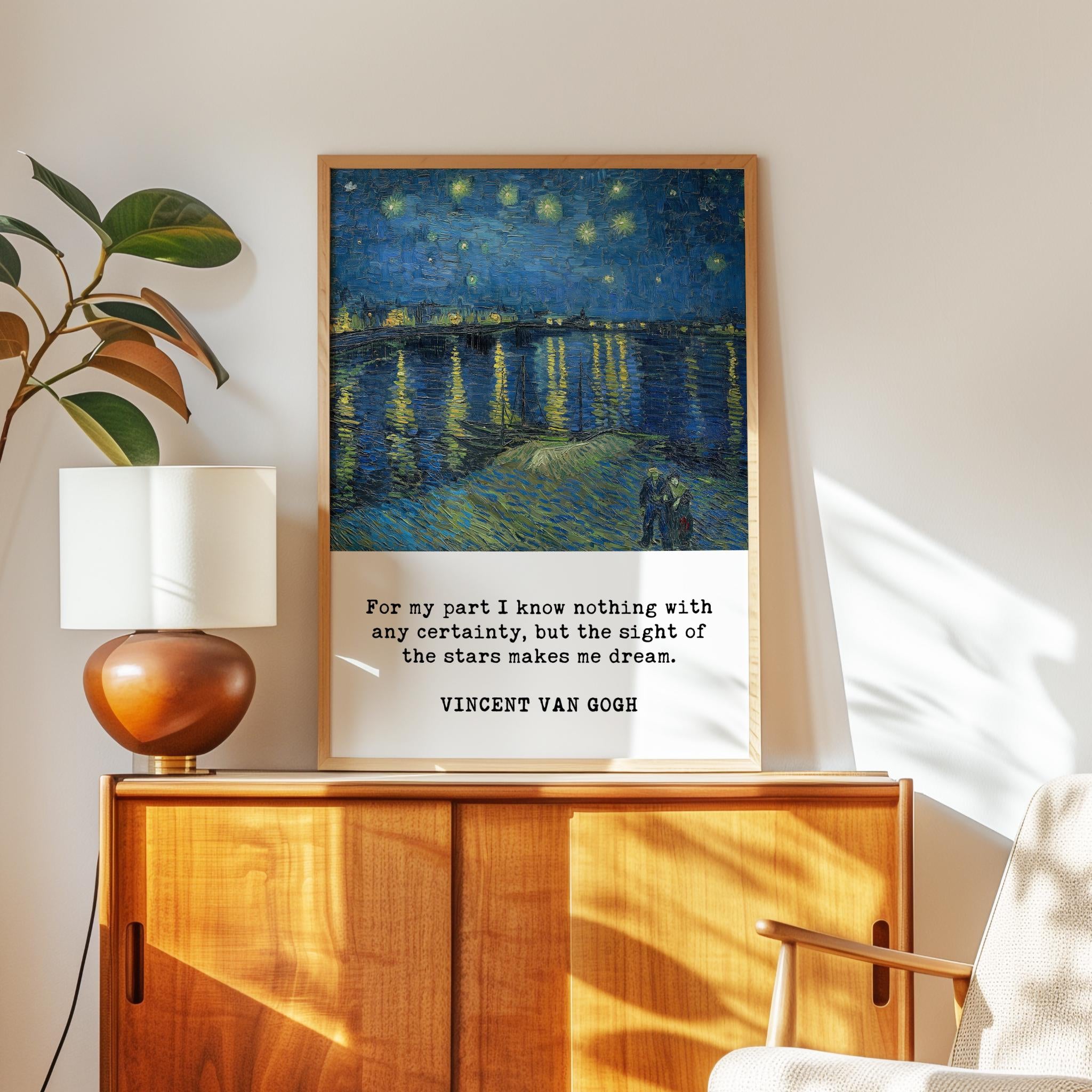 a framed painting of a starry night sky over a body of water, with a quote by Vincent Van Gogh below it. The painting is displayed on a wooden cabinet, and there is a lamp and a plant in the background.