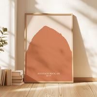 a framed print of a large orange shape, placed on a wooden floor next to a stack of books.