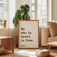 a framed quote by Seneca, "He who is brave is free", placed in a living room setting with a potted plant and a window.