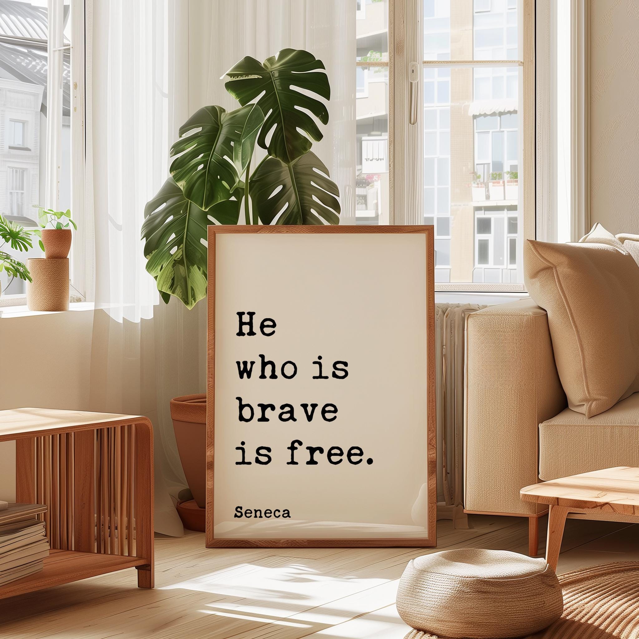 a framed quote by Seneca, "He who is brave is free", placed in a living room setting with a potted plant and a window.