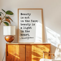 a framed quote by Daniel Gibson that reads "Beauty is not in the face; beauty is a light in the heart." The quote is displayed on a wooden cabinet or dresser, with a lamp and a plant nearby.
