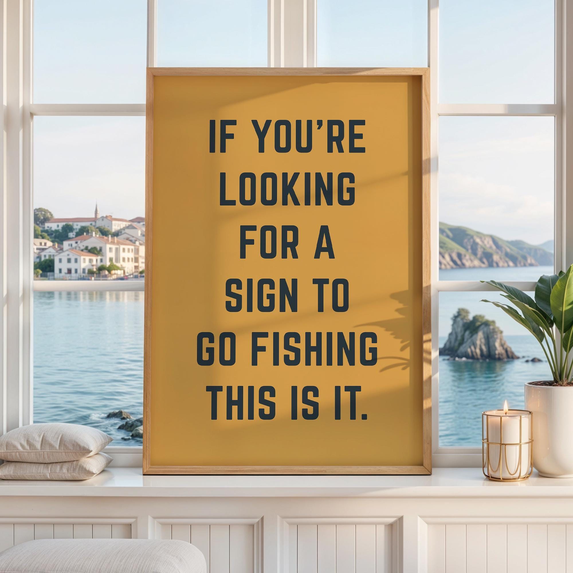 May include: A rectangular wall art print in a light wood frame featuring a mustard yellow background with bold black text that reads: IF YOU'RE LOOKING FOR A SIGN TO GO FISHING THIS IS IT. The print is displayed against a bright window backdrop.